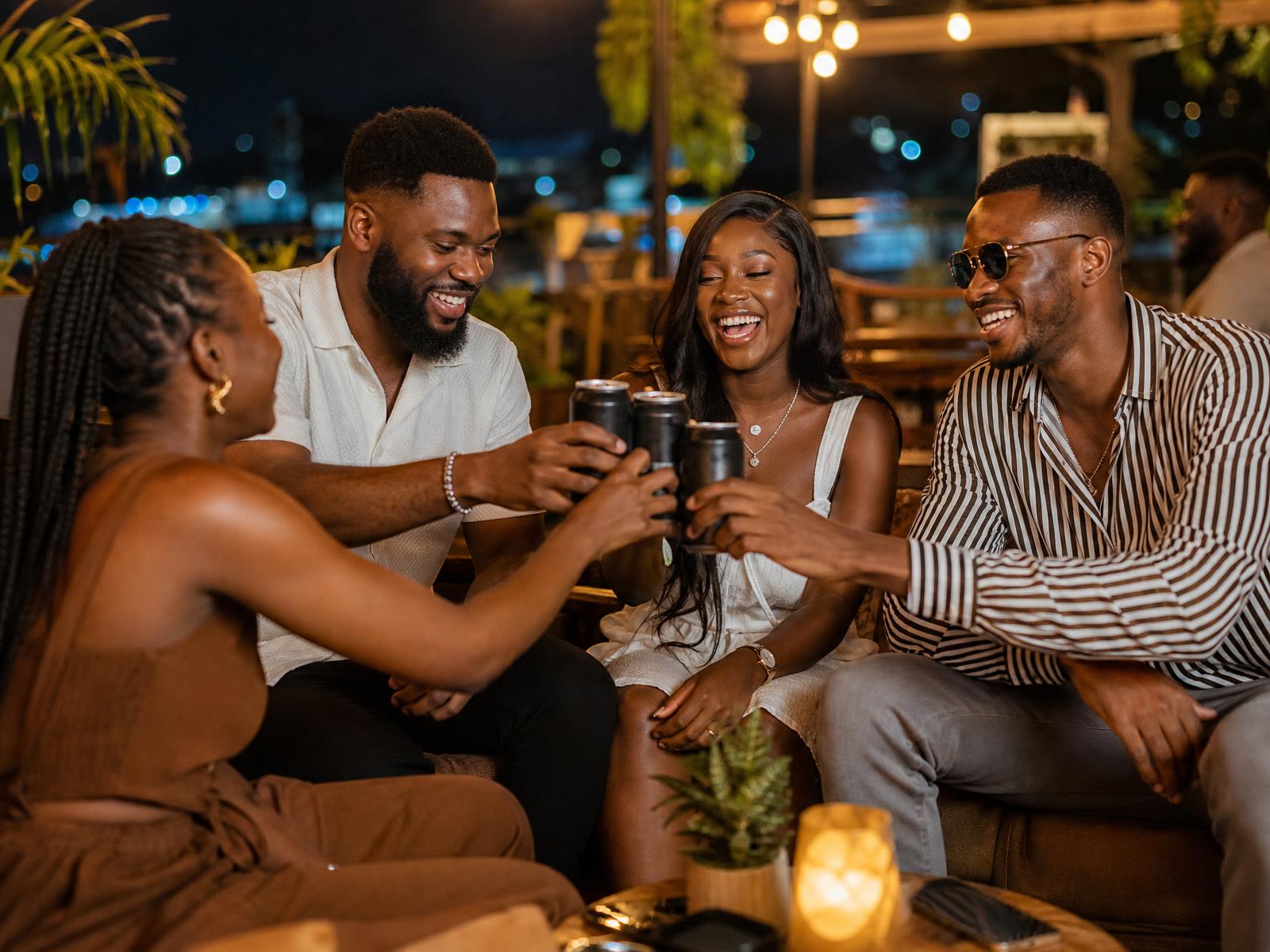 Friends laughing around a table with cans of cocktails in an ice bucket at night